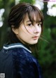 A young woman in a blue jacket standing in the woods.