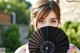 A woman holding a black fan in front of her face.